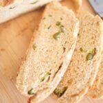 2 slices of artisan bread with peppers throughout on a wooden board.