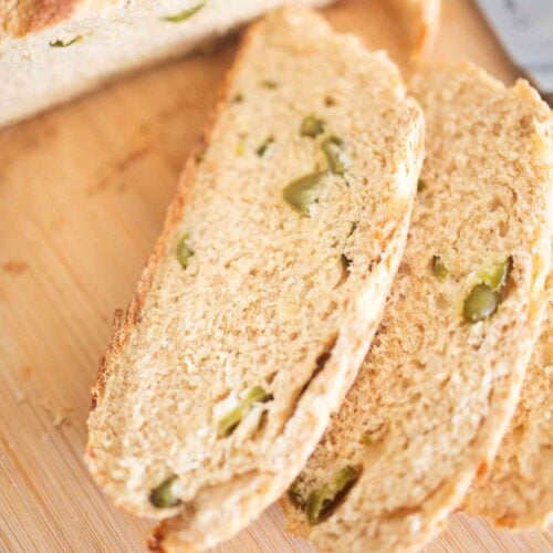 2 slices of artisan bread with peppers throughout on a wooden board.