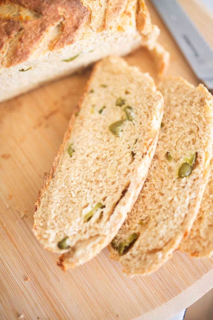 2 slices of artisan bread with peppers throughout on a wooden board.
